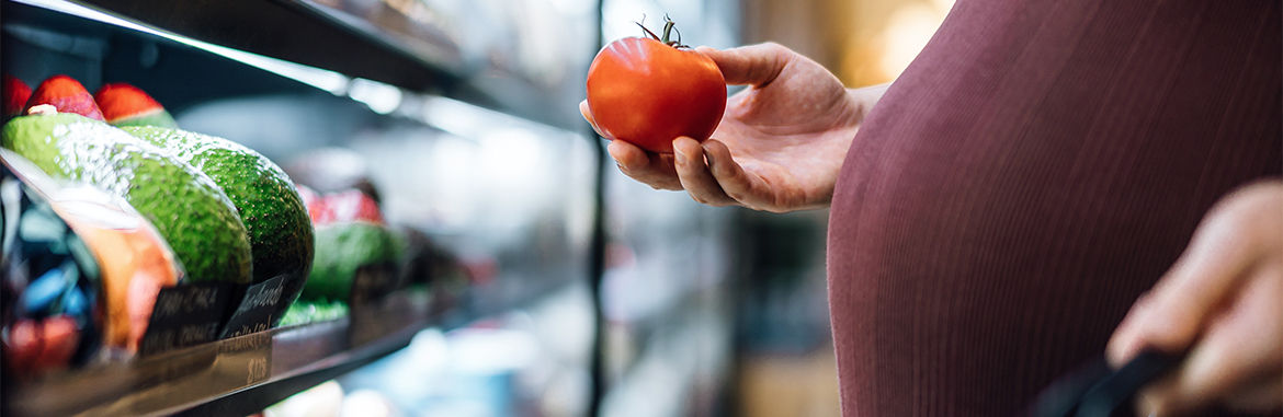 Cropped shot of pregnant woman grocery shopping in supermarket, shopping for fresh and healthy fruits and vegetables. Choosing tomato. Eating well with balanced nutrition. Pregnancy health and wellness. Healthy eating habit and lifestyle during pregnancy