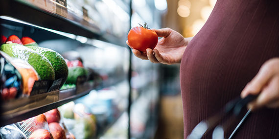 Cropped shot of pregnant woman grocery shopping in supermarket, shopping for fresh and healthy fruits and vegetables. Choosing tomato. Eating well with balanced nutrition. Pregnancy health and wellness. Healthy eating habit and lifestyle during pregnancy