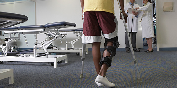 A man with a knee brace walking with crutches