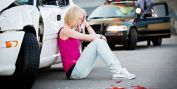 A woman sits in pain next to her car after an accident