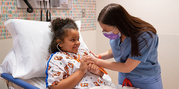 A young girl listens to her own heart through a stethoscope while receiving care from a doctor