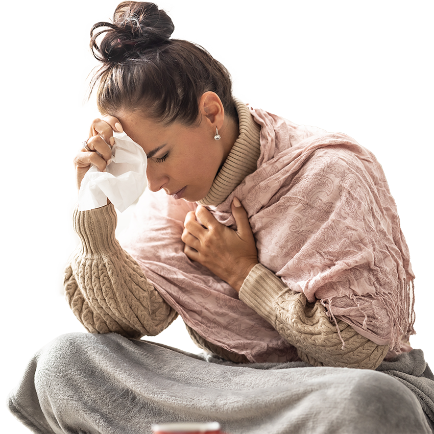 A woman sits under blankets with a tissue, holding her forehead and chest