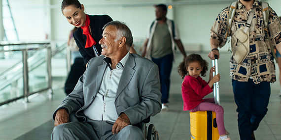 A man in a wheelchair looks up at a flight attendant who is wheeling him through an airport