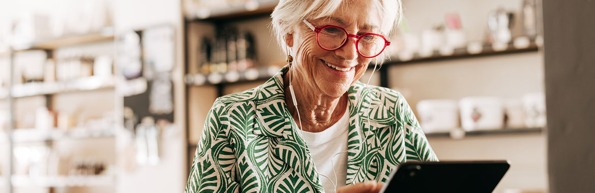 An older woman uses a tablet while sitting at a table with a cup of coffee