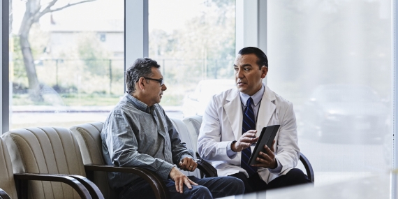 Doctor with digital tablet discussing with male patient in waiting room