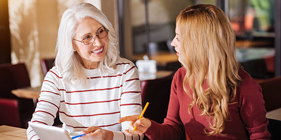 Two women, one older, the other younger, sit at a table discussing a document on a tablet