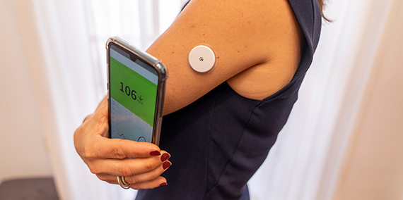 Una persona diabética usa su teléfono inteligente para leer el medidor de glucosa constante conectado a su brazo.