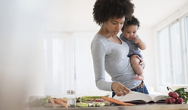 Madre sosteniendo a su hijo mientras mira un libro de cocina