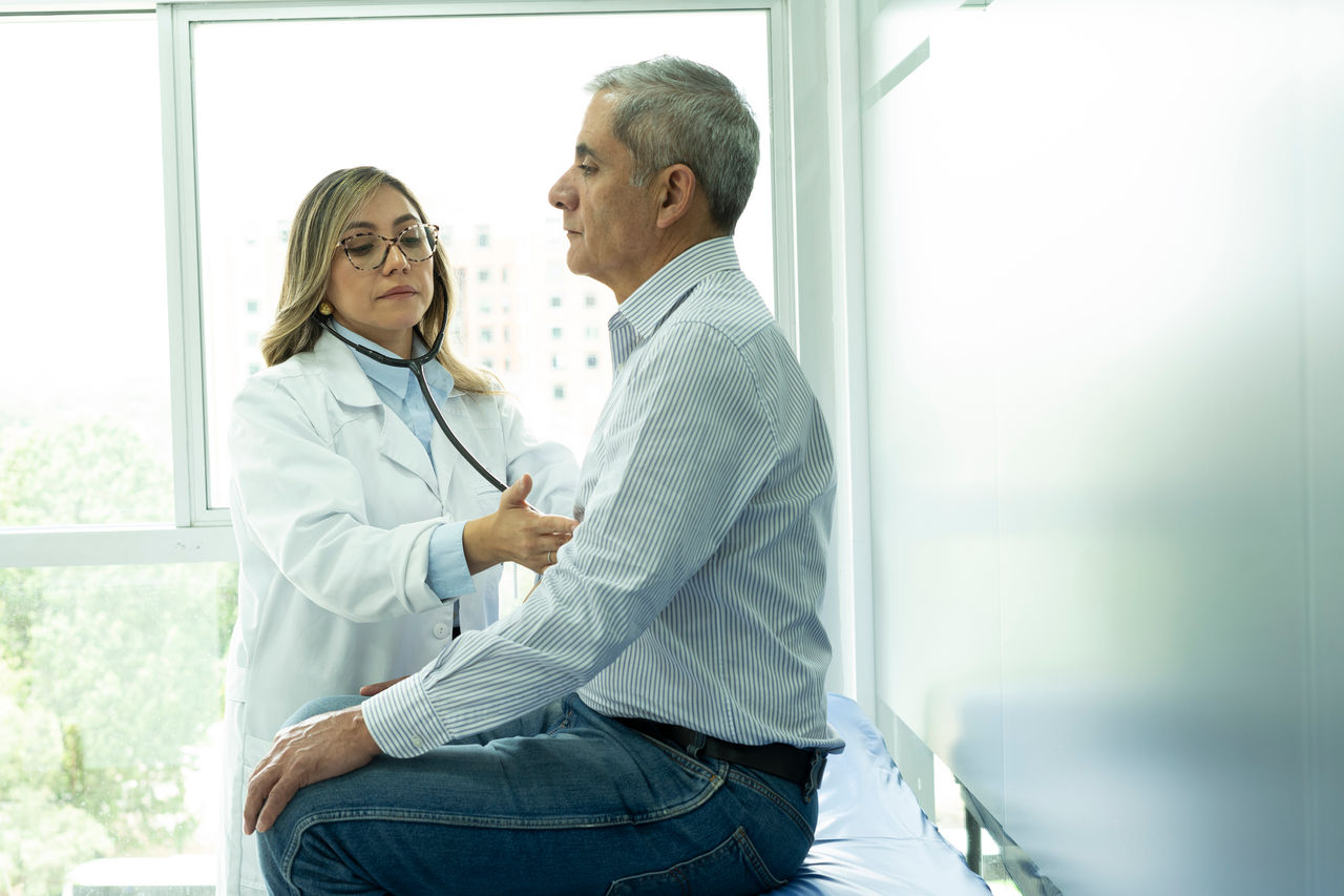 A female doctor uses a stethoscope to listen to the chest of a male patient