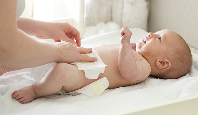 A nappy being put on a baby by and adult