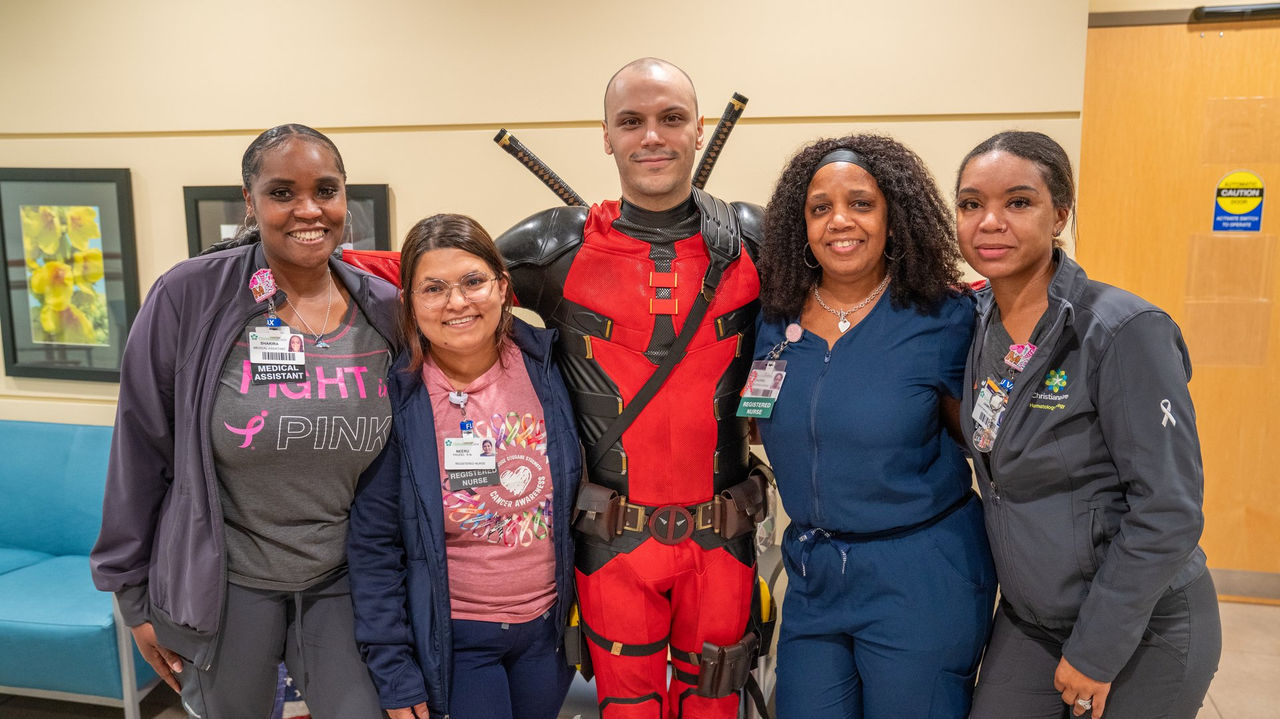 A patient in a Deadpool costume poses with four care team members at the cancer center bell-ringing celebration.