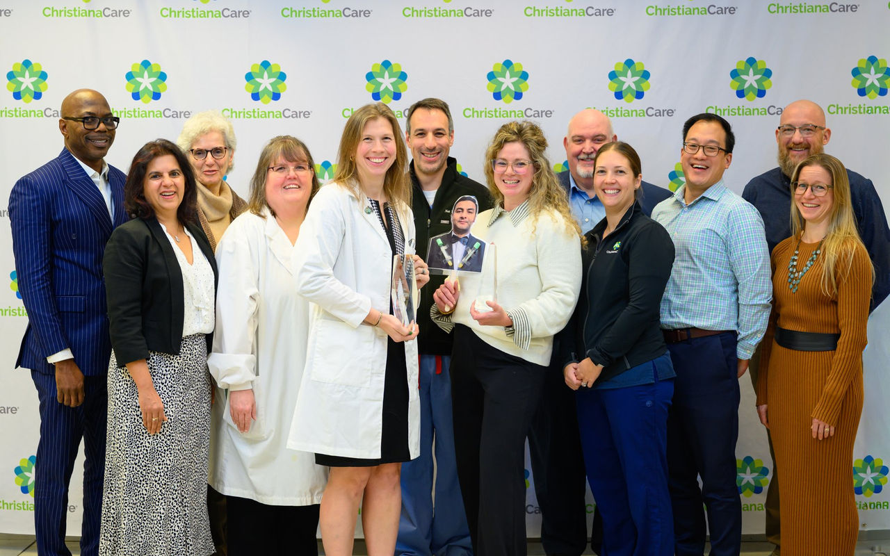 A large group of ChristianaCare colleagues poses with a crystal trophy in front of a branded backdrop at the Way Awards ceremony.