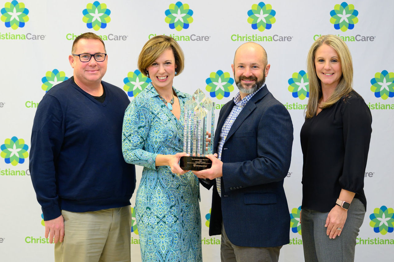 Four colleagues pose with a crystal Way Award trophy in front of a ChristianaCare step-and-repeat backdrop.