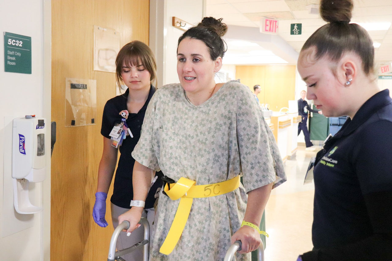 A patient walks with the support of two ChristianaCare team members guiding her steps.
