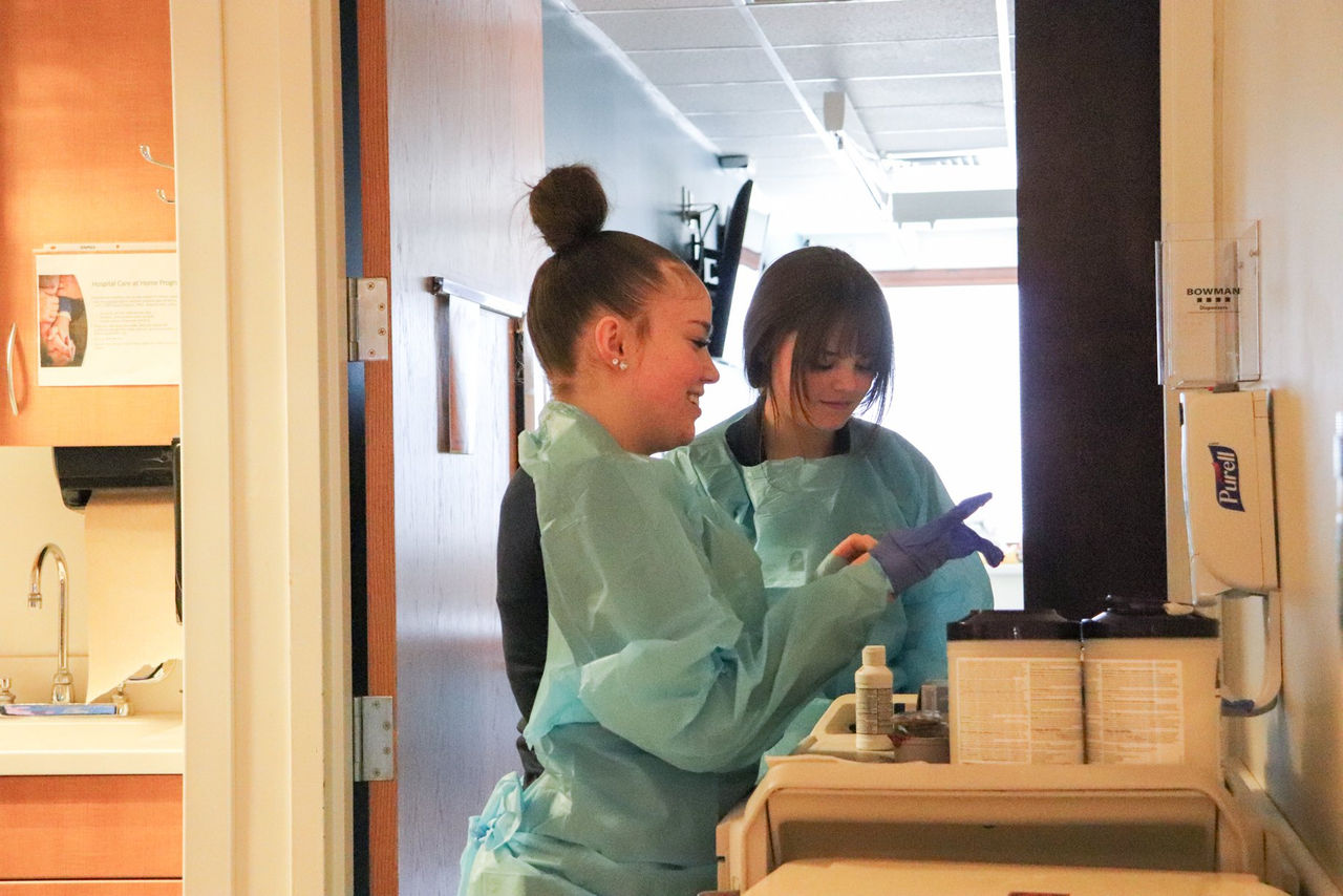 Two mobility interns in protective gowns prepare supplies in a patient care area.