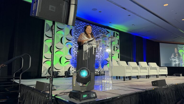 Arlene Daniels on stage at a lecturn, speaking at the National Food and Medicine Conference