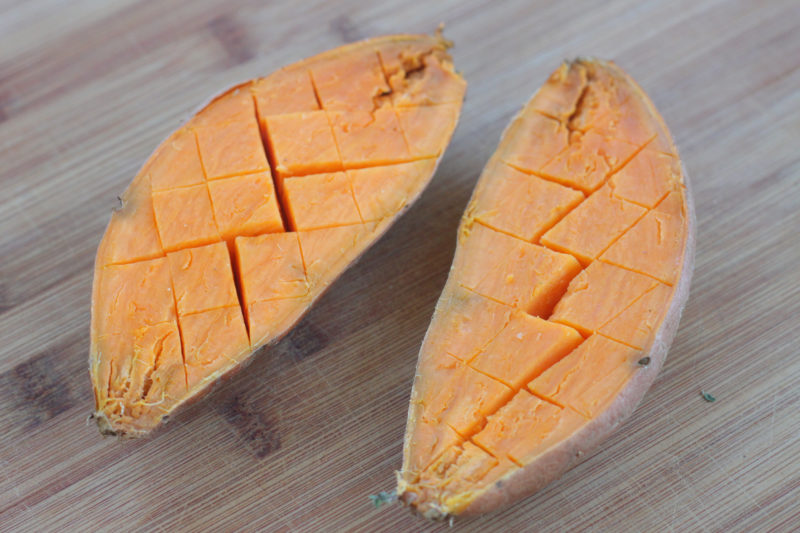A fresh sweet potato split in half and scored in a diamond pattern, prepped and ready to absorb butter, spices, or glaze during roasting for maximum flavor and easy serving.