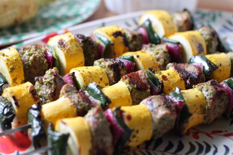 Colorful grilled skewers featuring marinated pork, yellow squash, zucchini, and red onion, cooked to perfection and served as a flavorful barbecue dish.