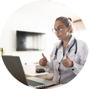 A female doctor holds both thumbs up while looking at a laptop computer